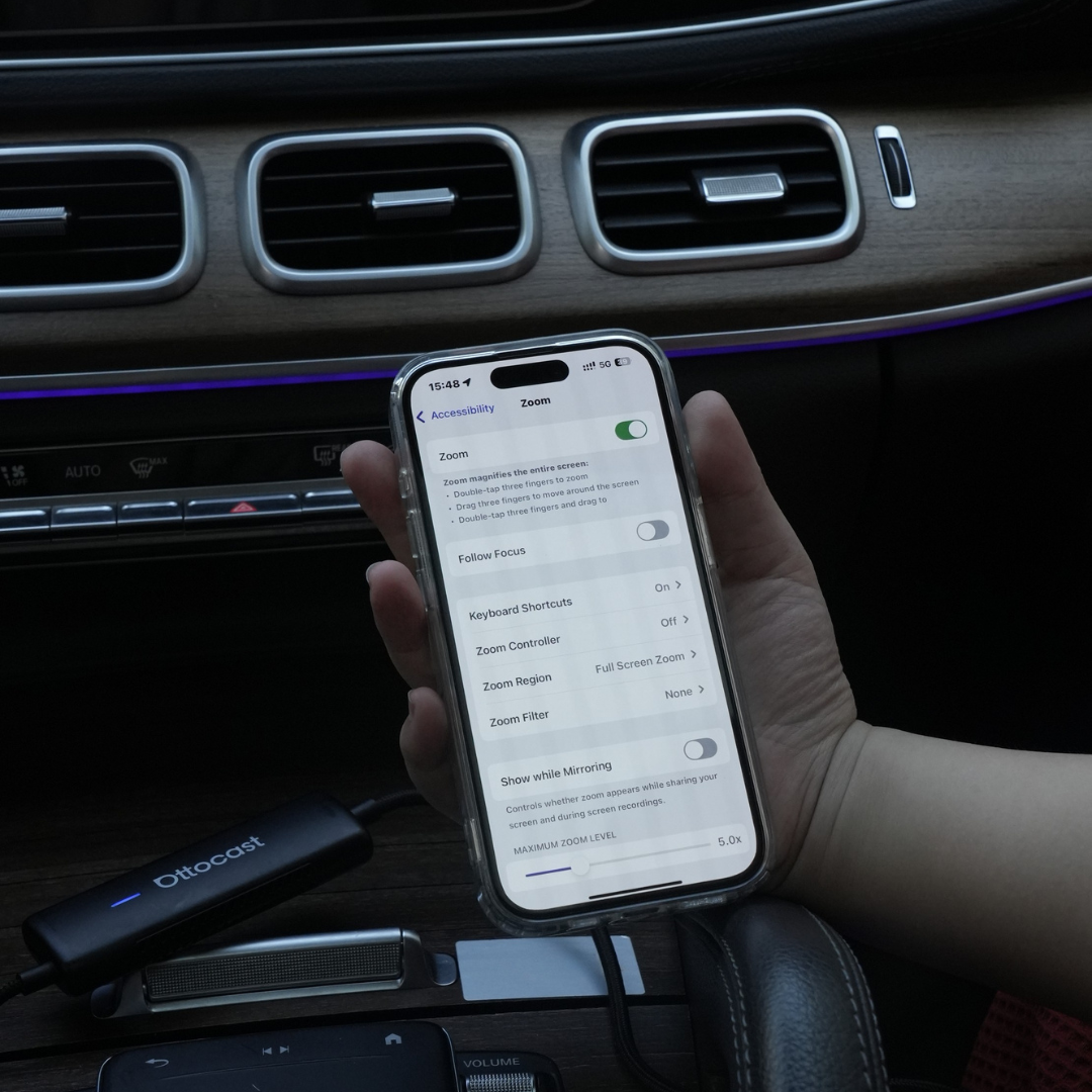 Hand holding iPhone connected to Ottocast wireless CarPlay adapter in car interior for seamless smartphone integration