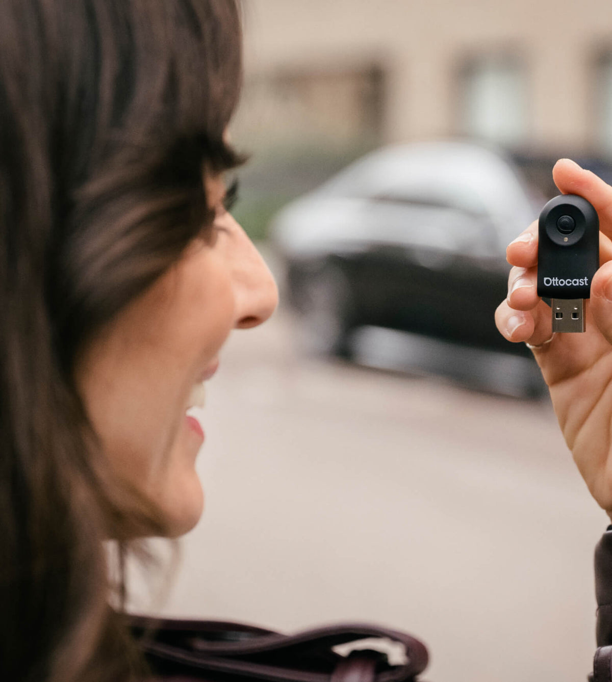 Woman holding Ottocast Mini wireless CarPlay and Android Auto adapter with compact USB design for easy in-car connection